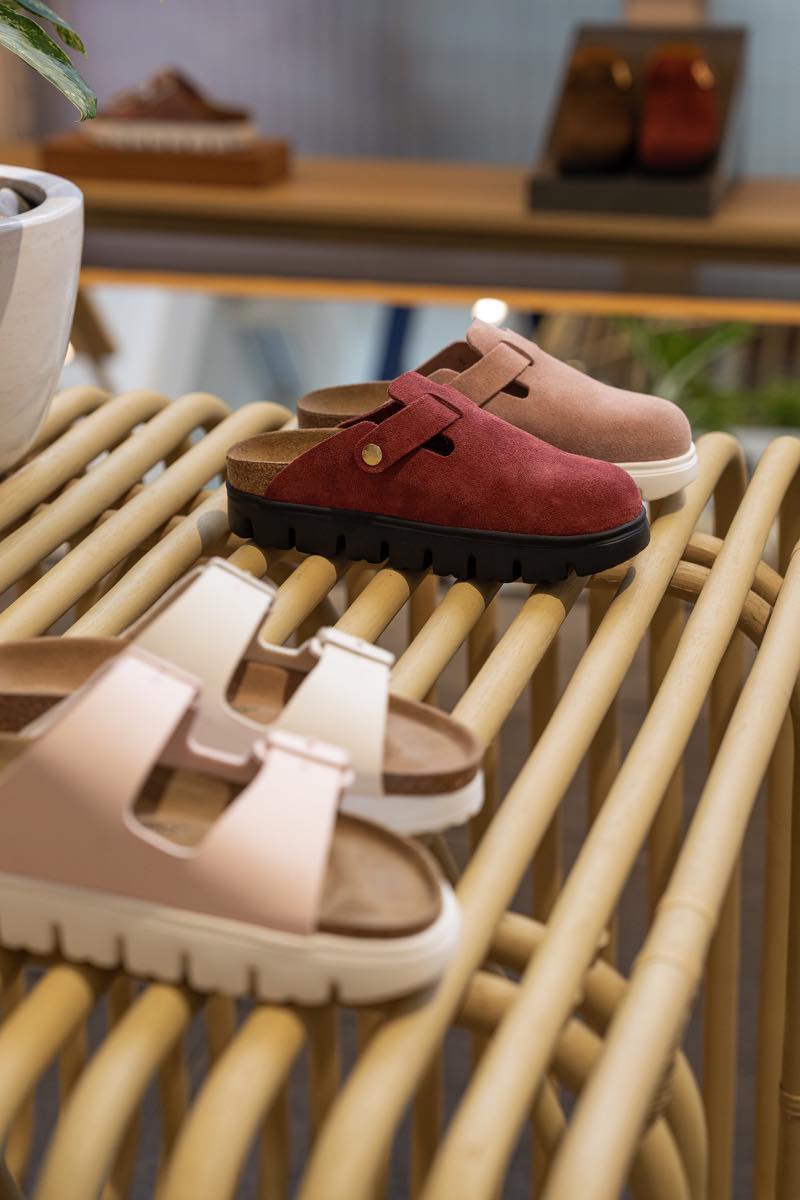 Suede clogs and leather sandals from BIRKENSTOCK displayed on a rattan bench inside the Ubud store