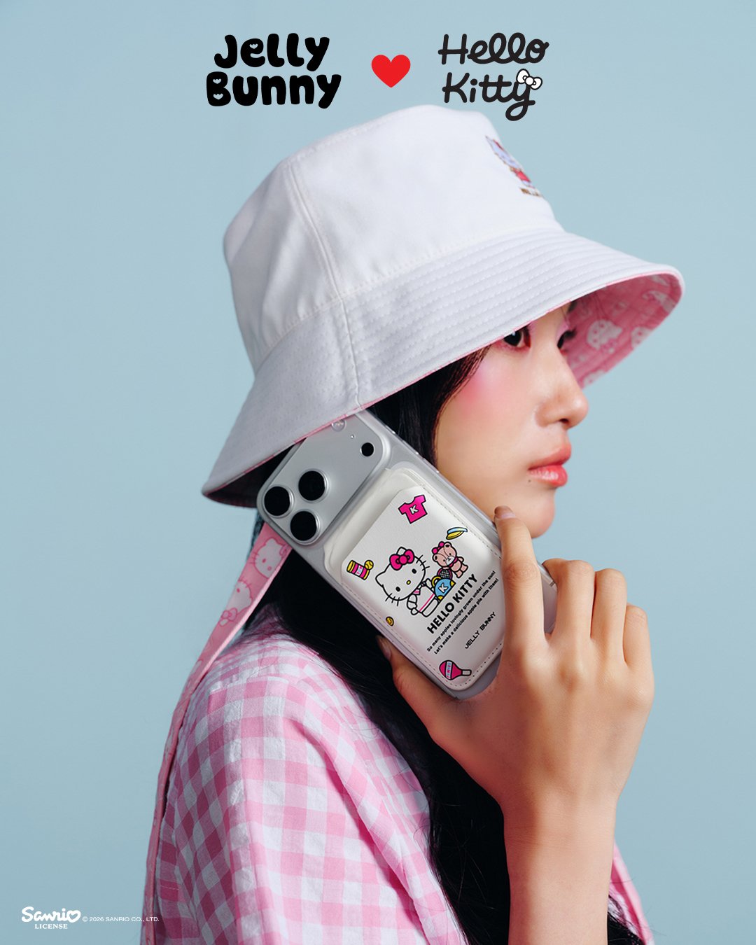 A model in a white bucket hat holds a phone in a Jelly Bunny x Hello Kitty printed case