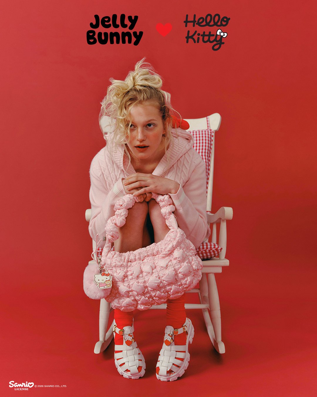 A model holds a pink quilted Jelly Bunny x Hello Kitty shoulder bag with a Hello Kitty charm, wearing white fisherman sandals