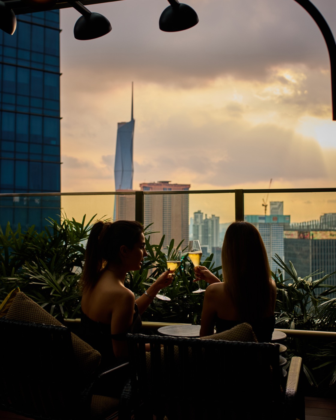 Guests with cocktails on the Four Siblings rooftop at Kimpton Naluria Kuala Lumpur, with the Kuala Lumpur skyline at sunset