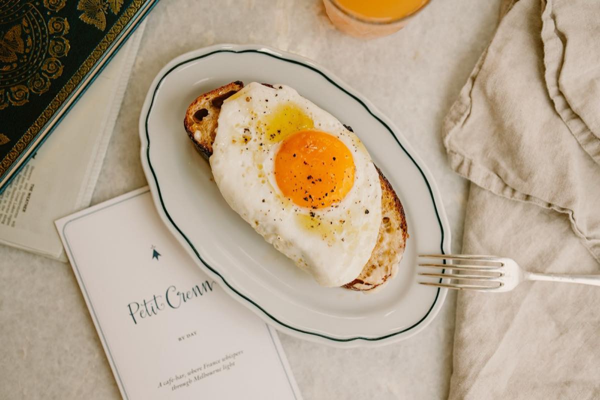 A croque madame on a plate beside the Petit Crenn menu