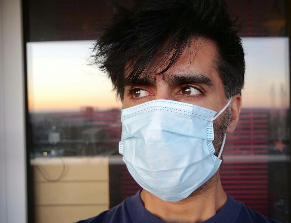 A man wearing a loose surgical mask by a window