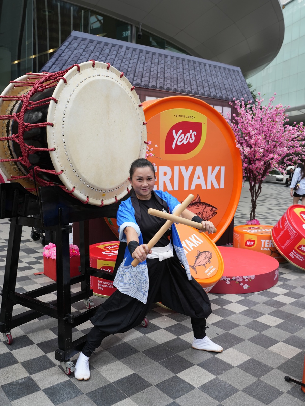 A taiko drummer in Japanese costume performs in front of giant Yeo's Teriyaki Tuna can props and cherry blossoms at the Bukit Bintang roadshow